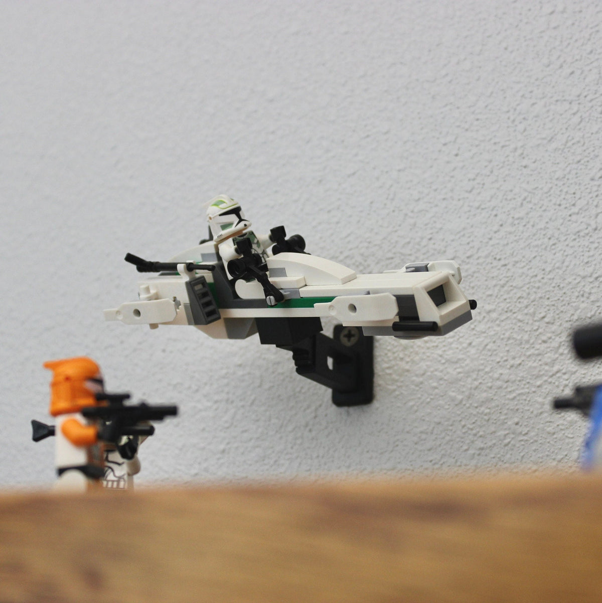 Small LEGO Star Wars speeder posed on the short black universal wall mount, with minifigures on a shelf below
