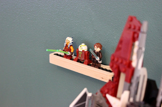 Four LEGO minifigures standing on the Baltic birch minifigure display next to a red LEGO ship on a dark wall